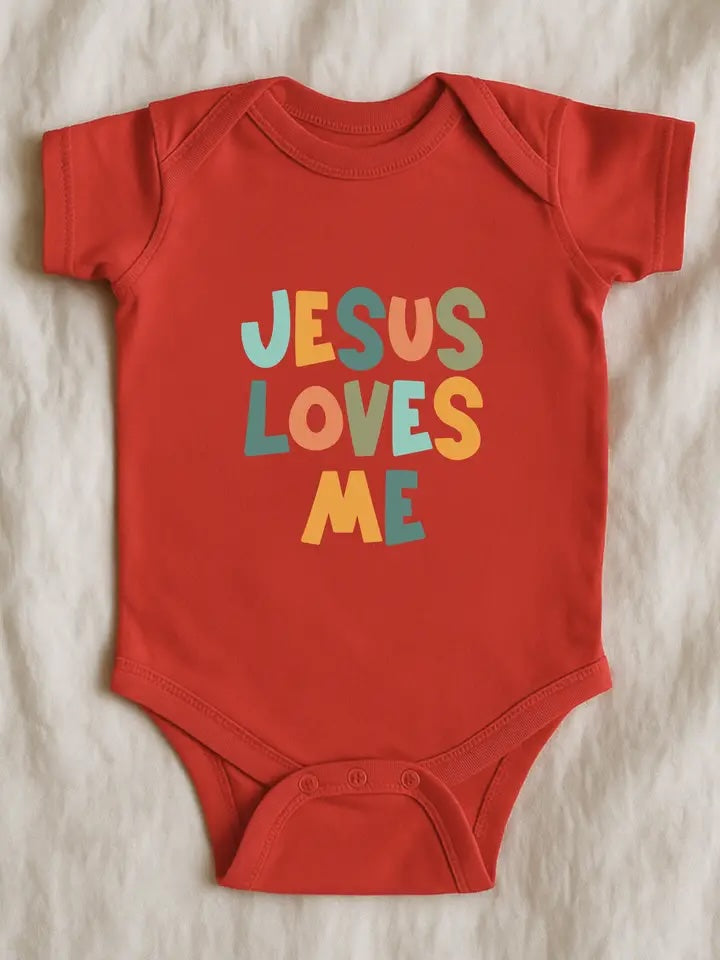 A red short-sleeve baby bodysuit laid flat on a textured white fabric background, featuring the phrase 'JESUS LOVES ME' printed in colorful retro-style letters.